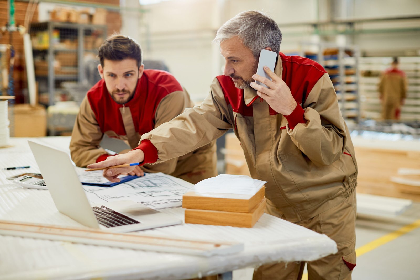 Home carpenter talking on the phone while using computer in a worksho