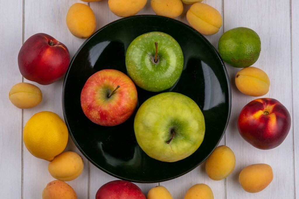 top view colored apples black plate with apricots peaches white surface